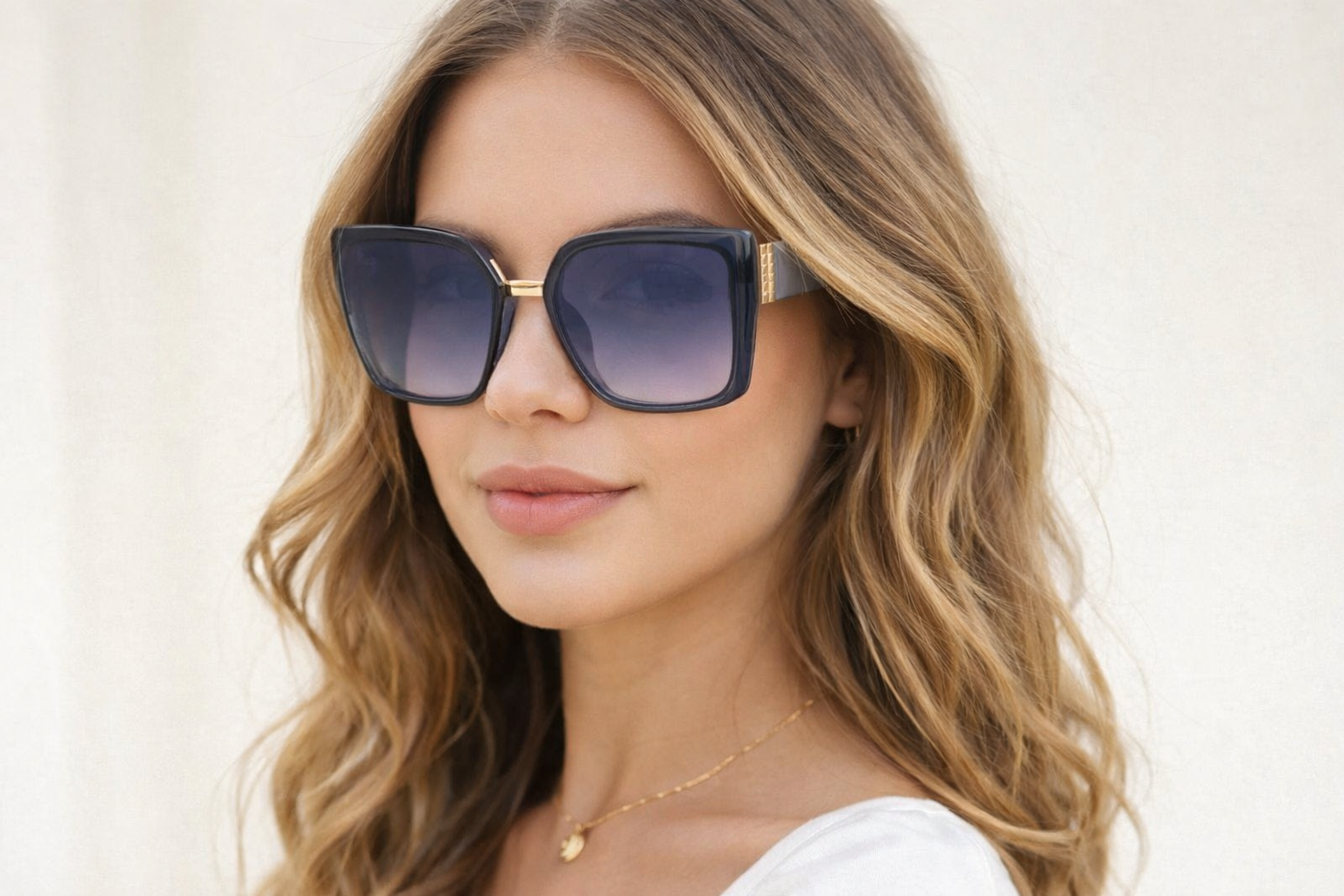 Woman wearing large black sunglasses with grey and gold accents against a plain white background