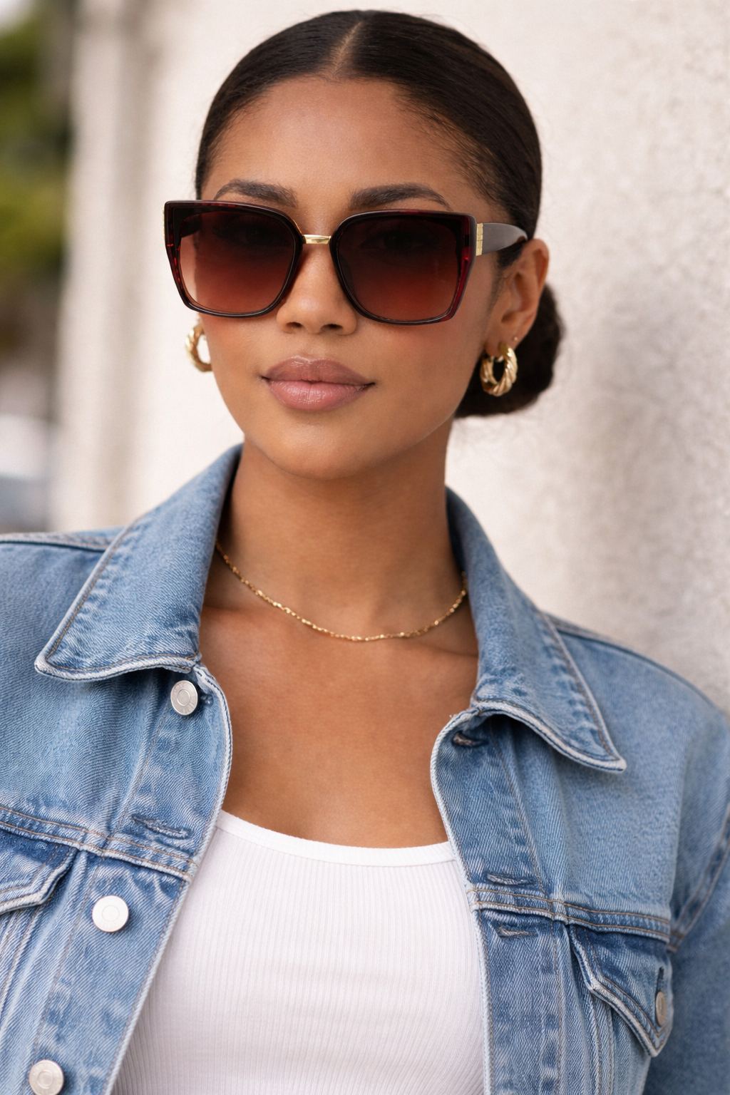 Woman wearing sunglasses and a denim jacket with a blurred white wall background