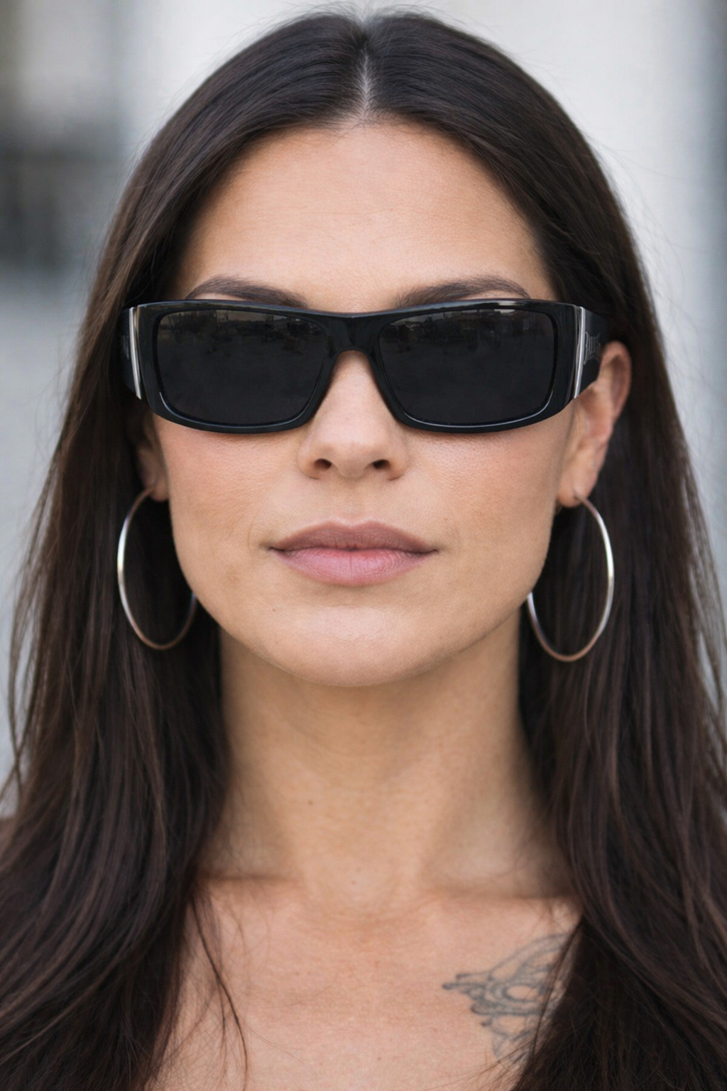 Woman wearing black sunglasses and hoop earrings with a blurred background